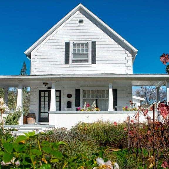 White farmhouse with porch and blooming garden