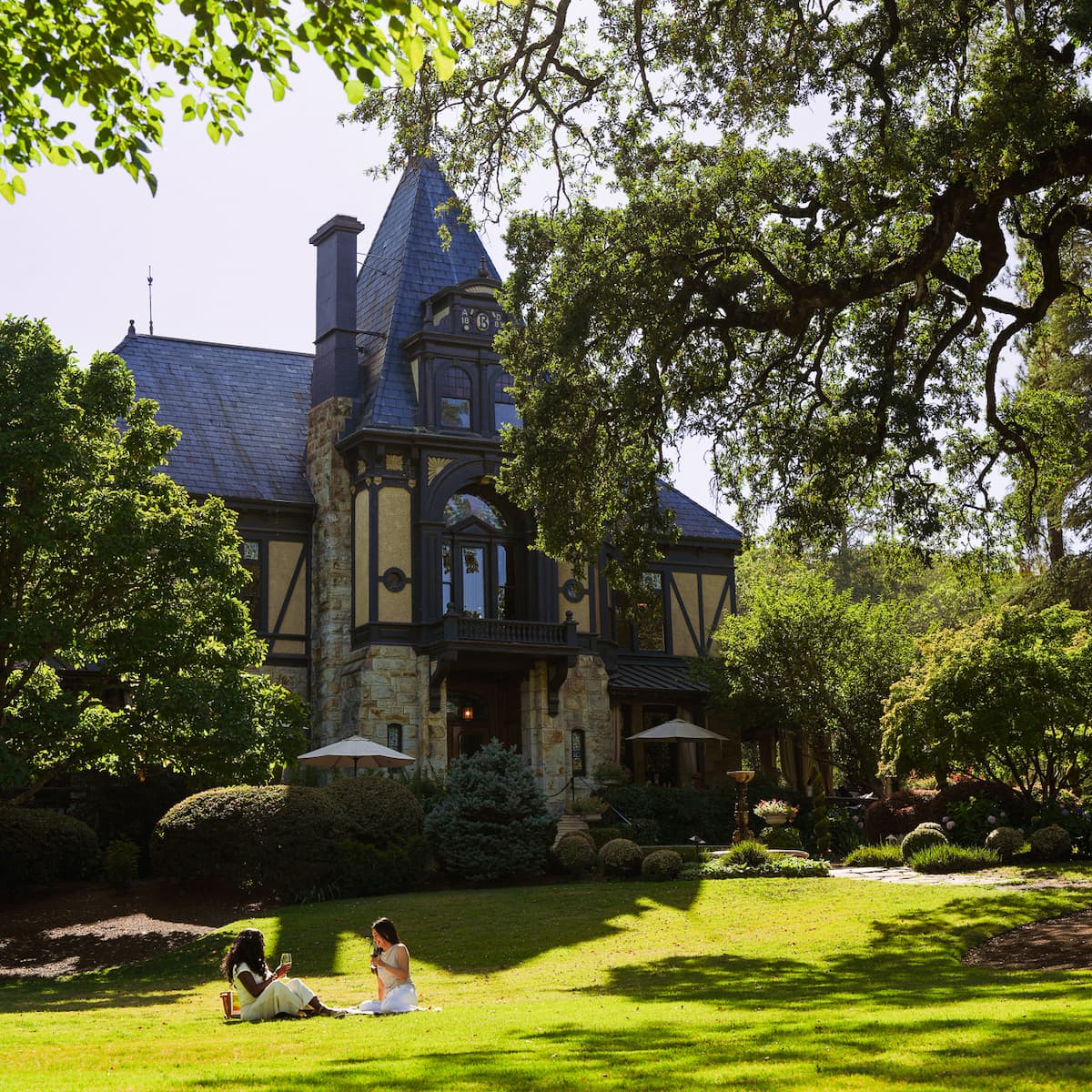 Two women picnic on lawn before large mansion