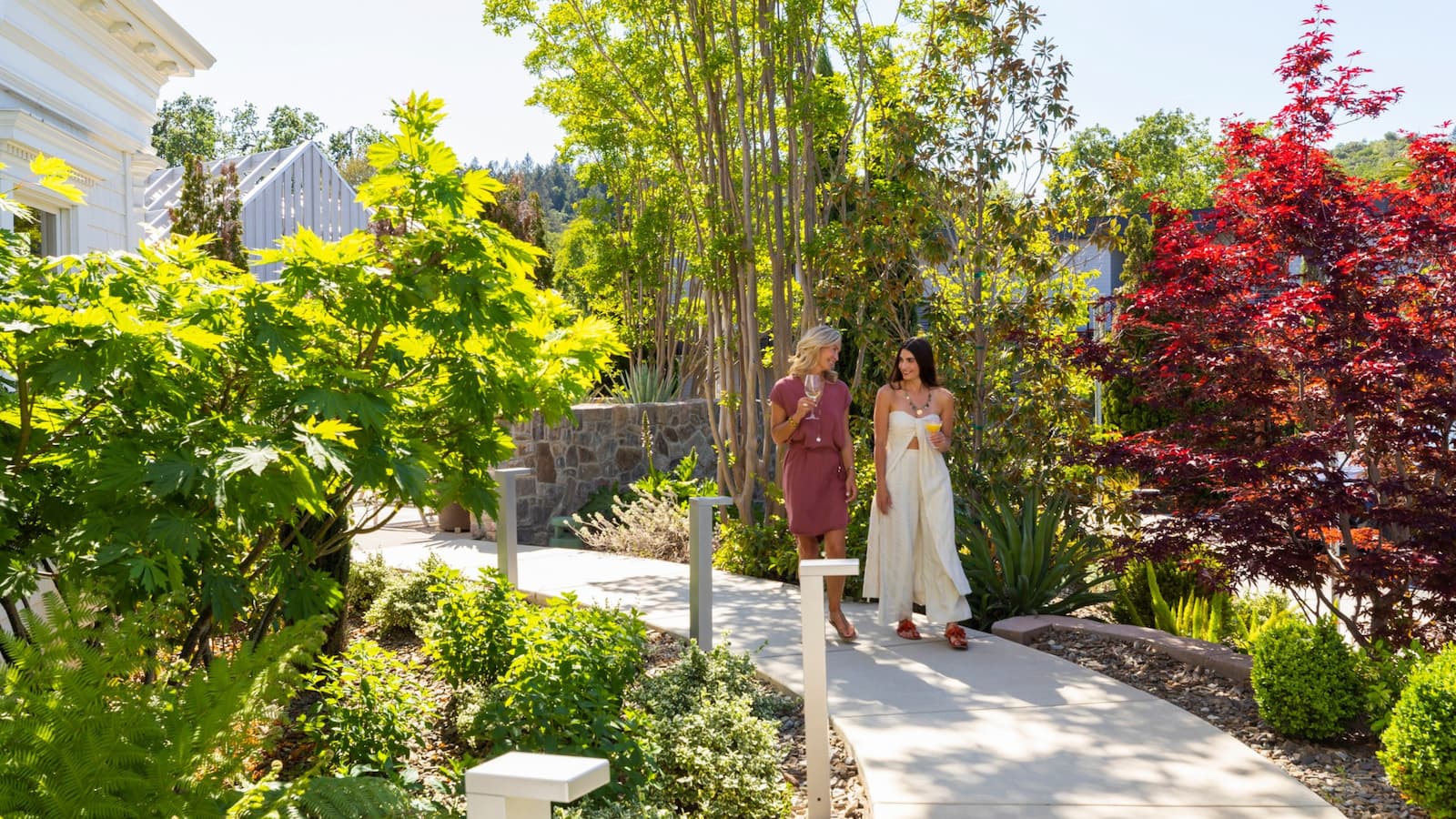 Two women walking in a lush garden.