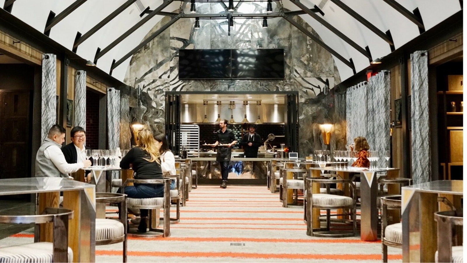 Elegant restaurant with seated patrons and open kitchen.