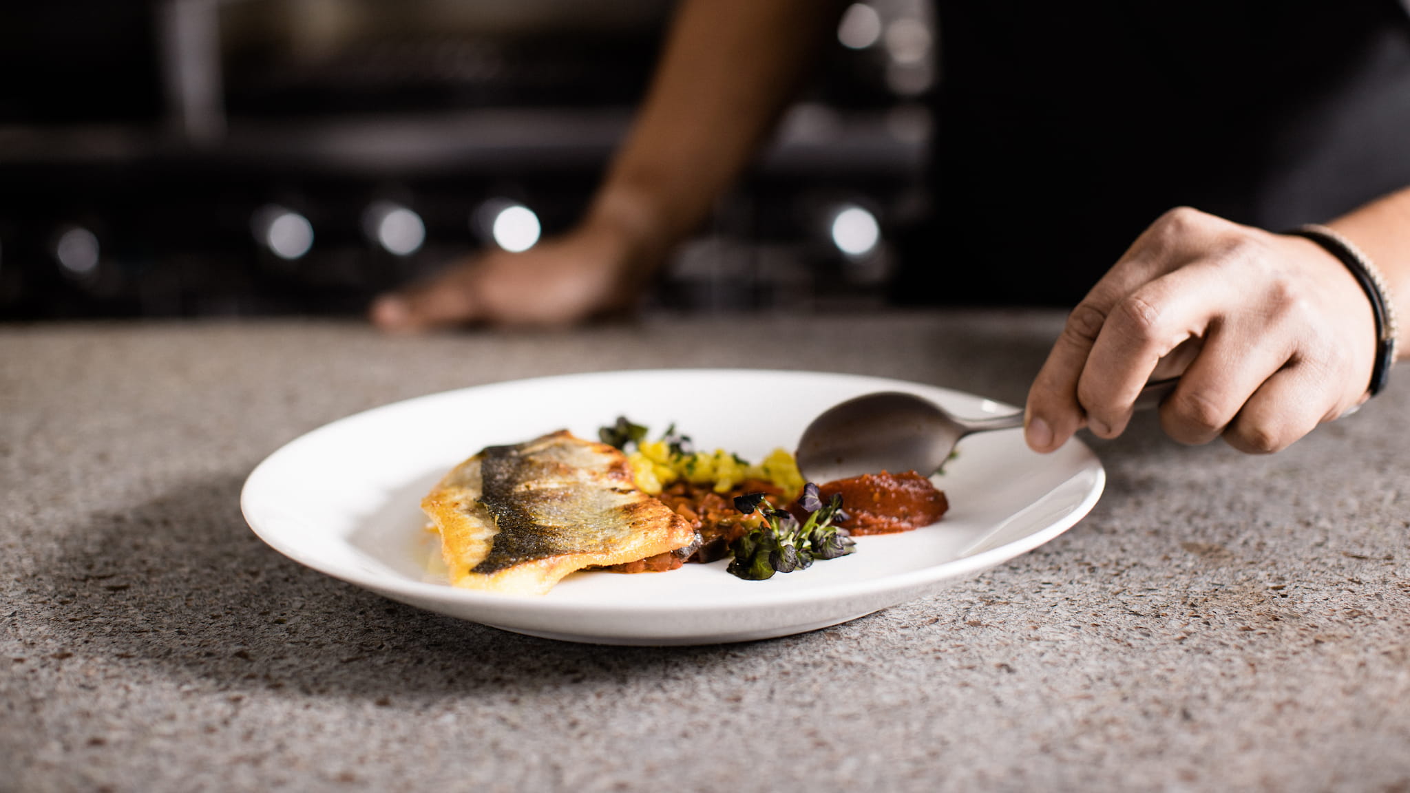 Person plating fish with sauce and vegetables