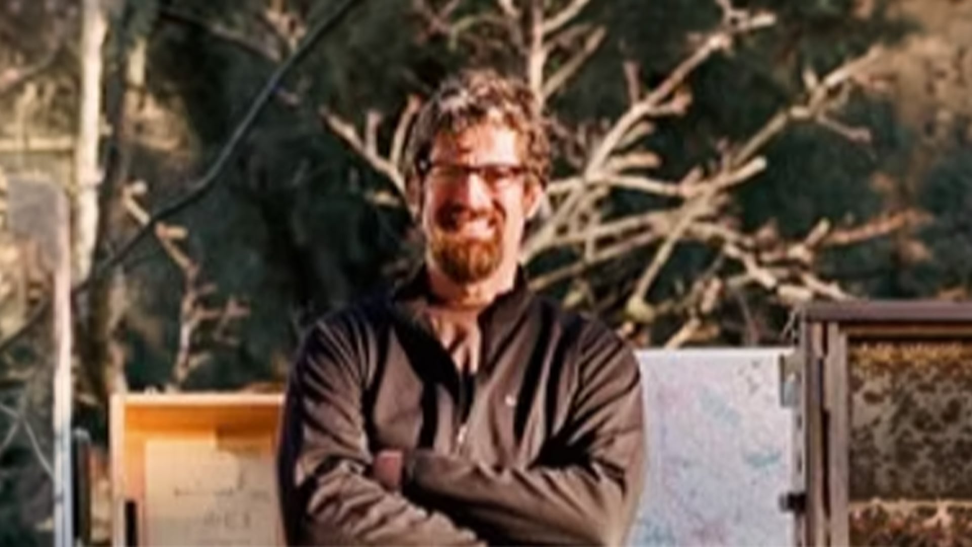 Bearded man with glasses standing near beehives outdoors