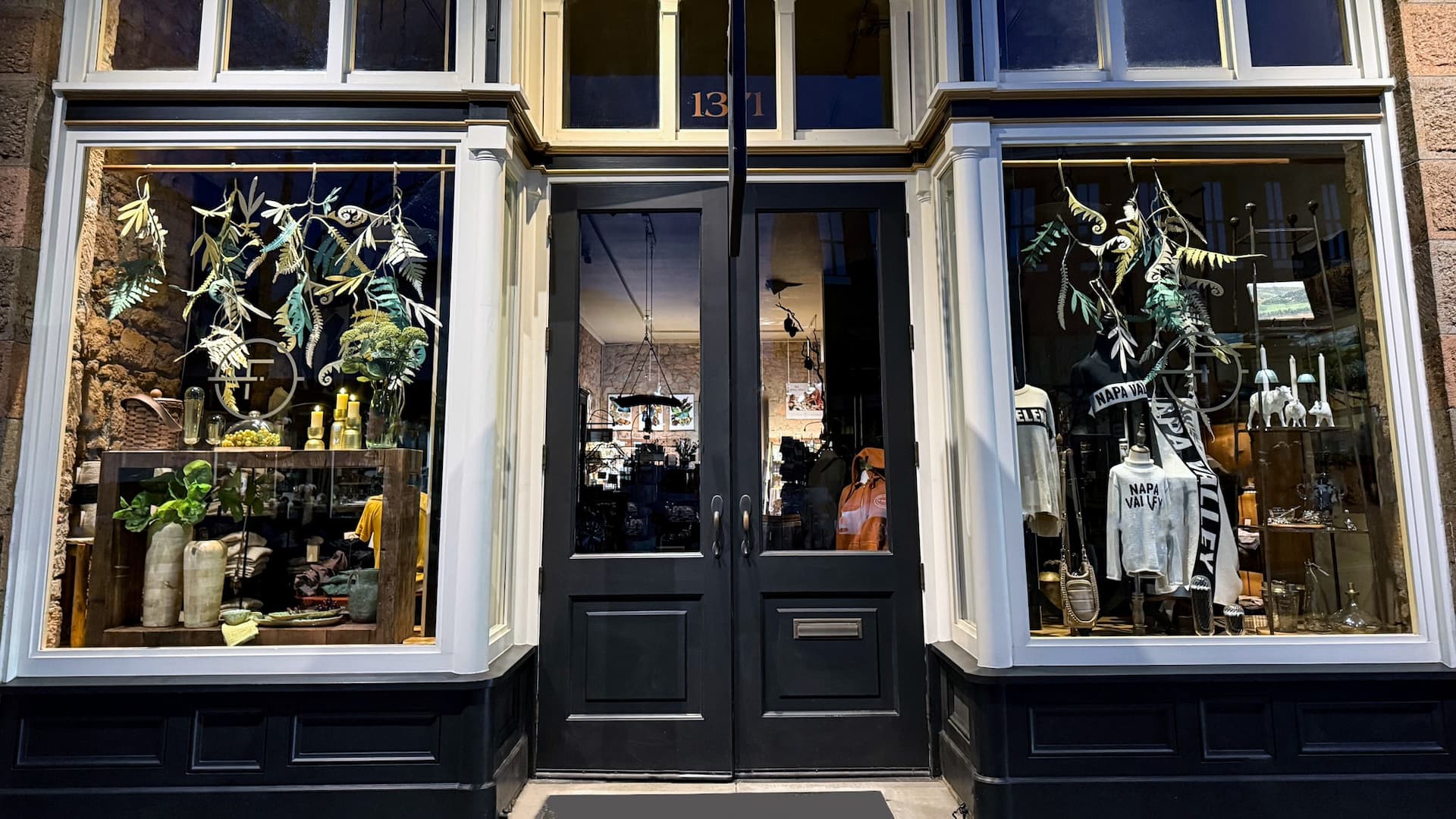 Storefront with plants and clothing display in windows.