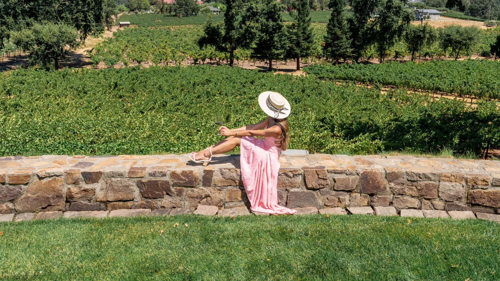 Woman in pink dress overlooking vineyard from stone wall