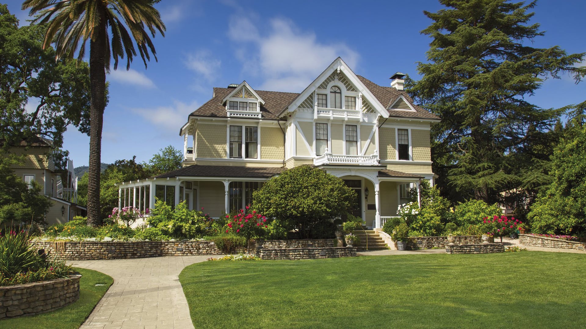 Victorian house with lush garden, lawn, and palm tree