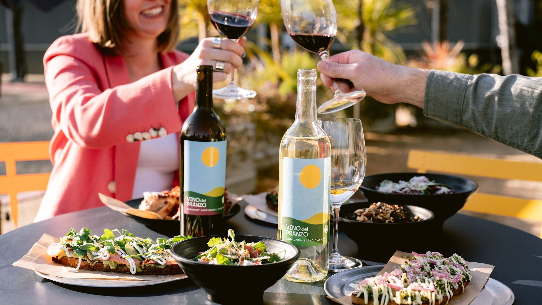 People toasting with wine outdoors and food on table.