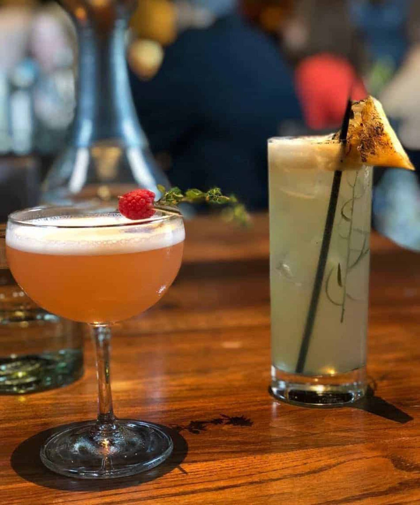Two cocktails on a wooden table, garnished elegantly.