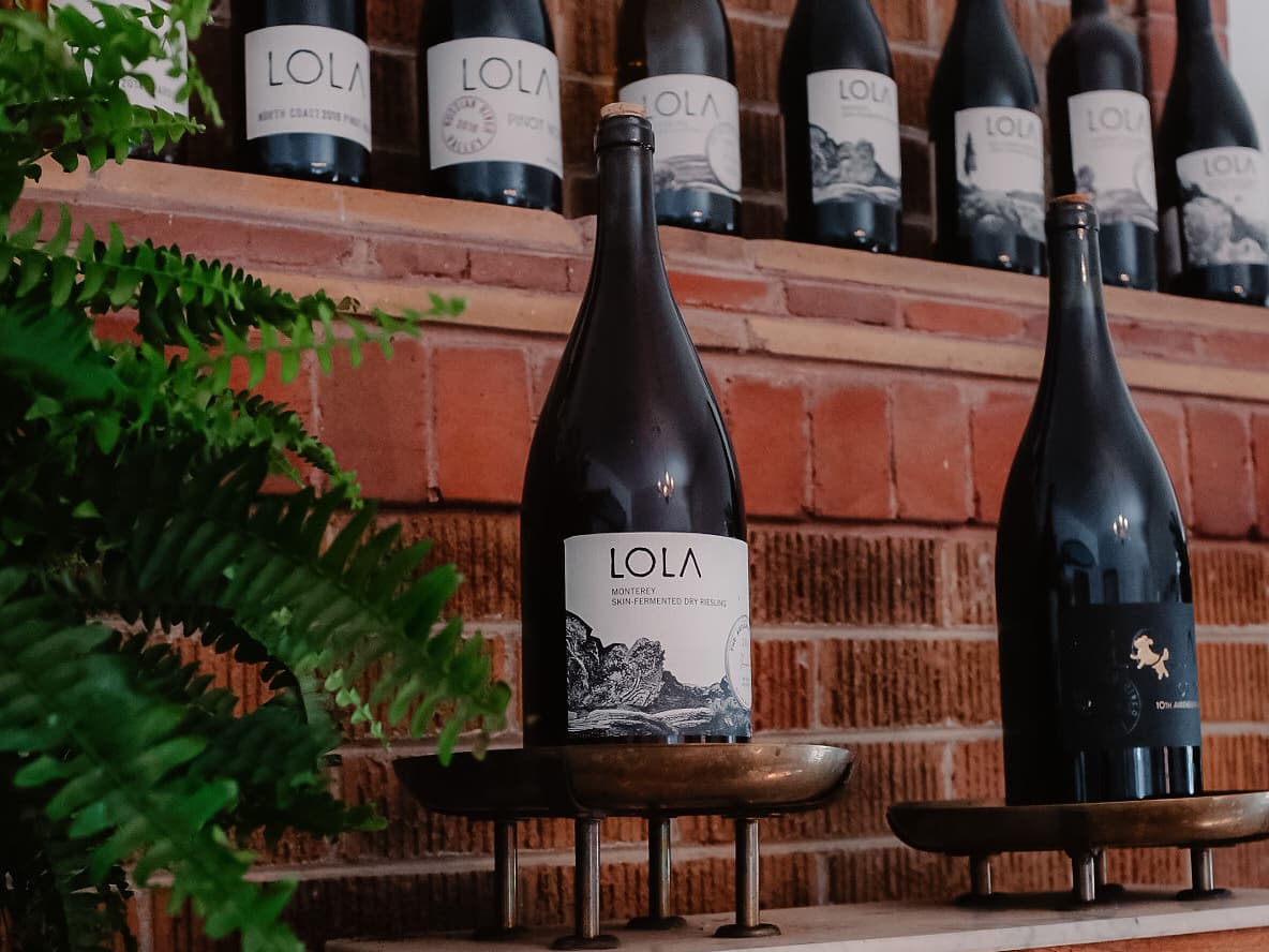 LOLA wine bottles displayed against brick wall