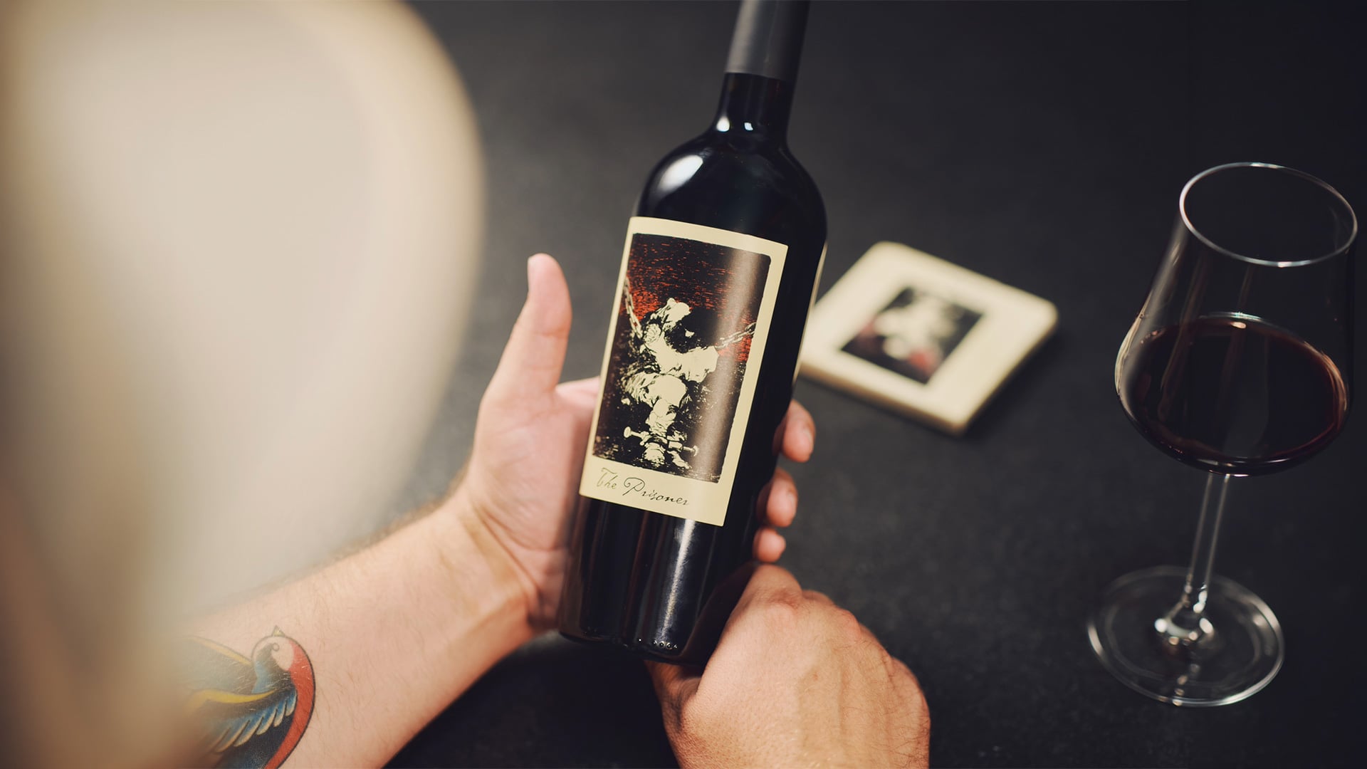 Person holding red wine bottle beside filled wine glass