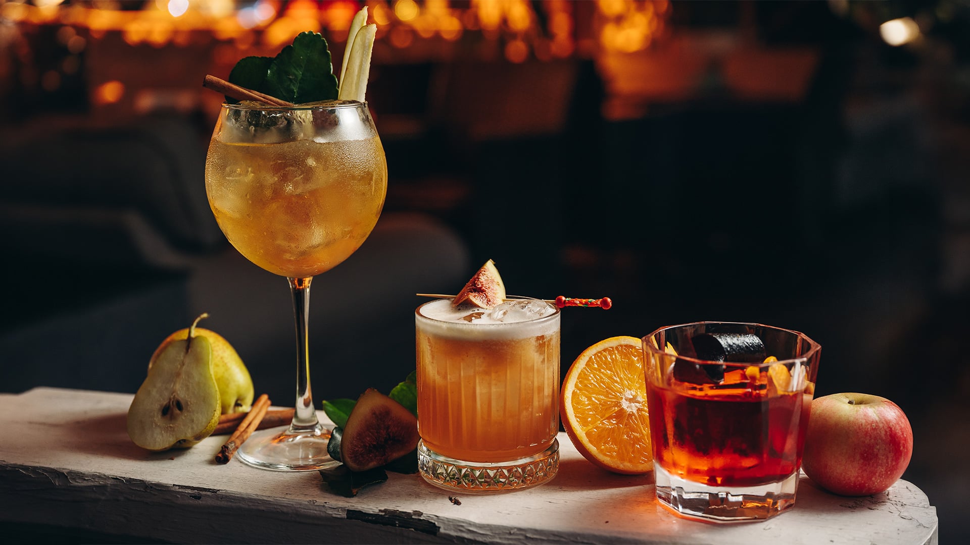 Three autumn cocktails garnished with fresh fruit and spices