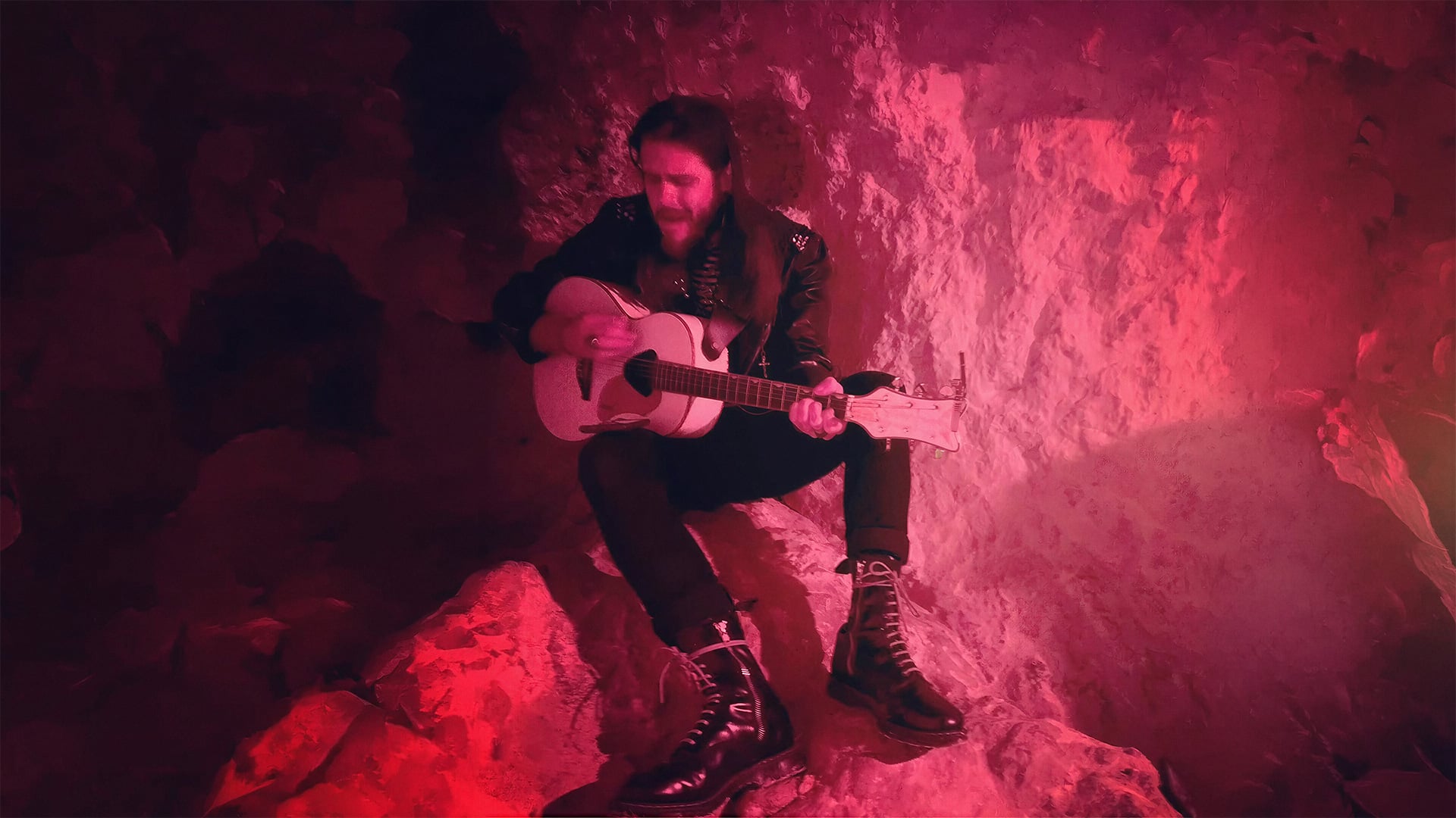 Man playing acoustic guitar in red-lit rocky cave