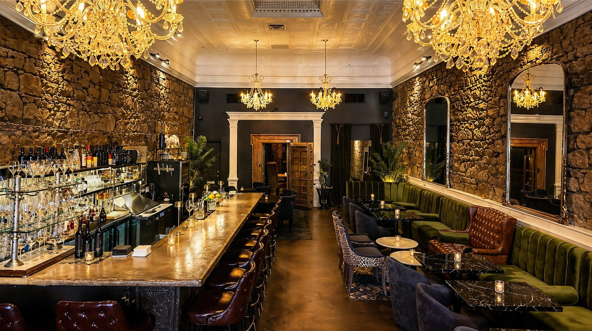 Elegant stone-walled bar with chandeliers and green velvet seating