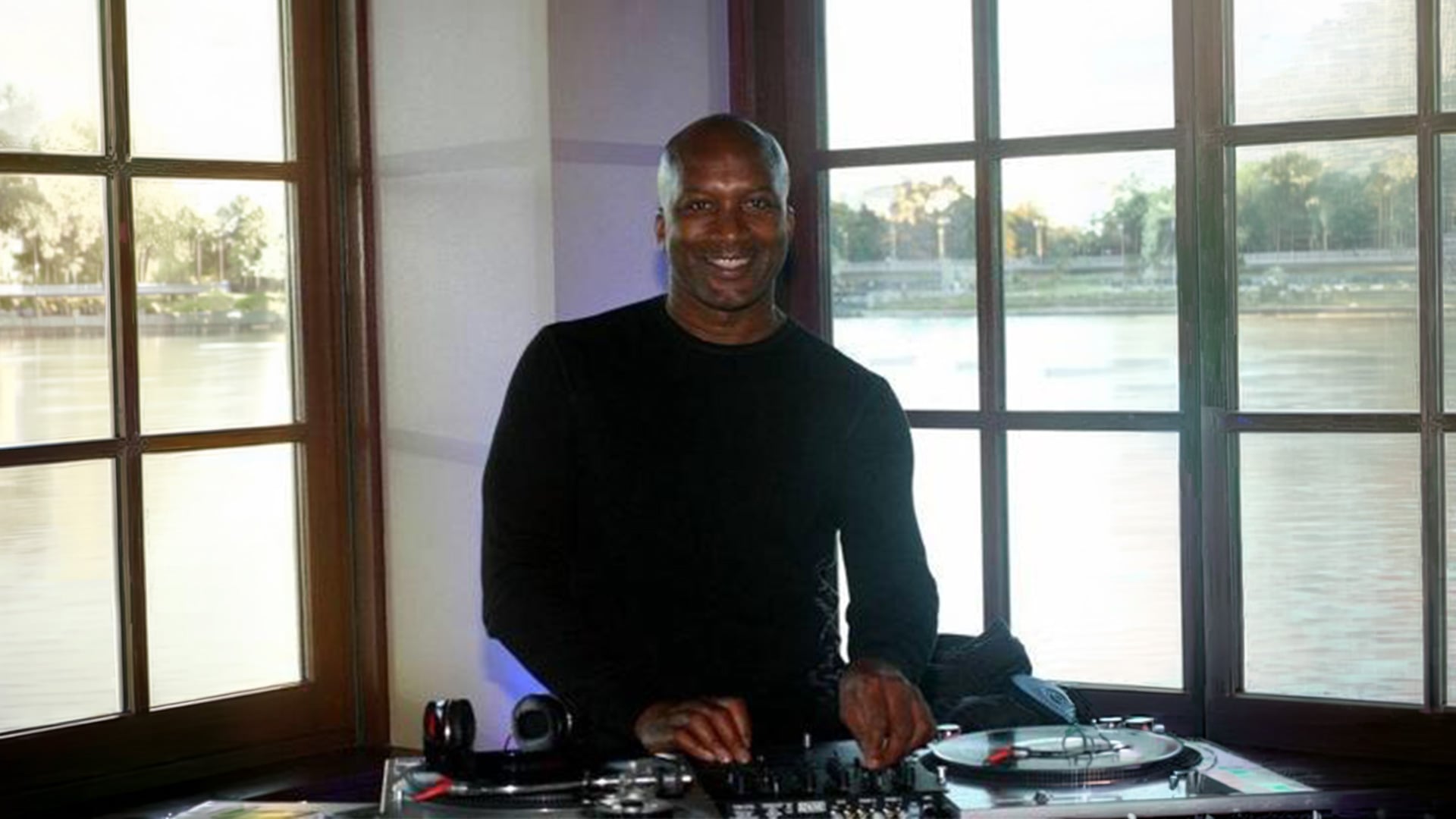 Smiling DJ mixing records beside large waterfront windows