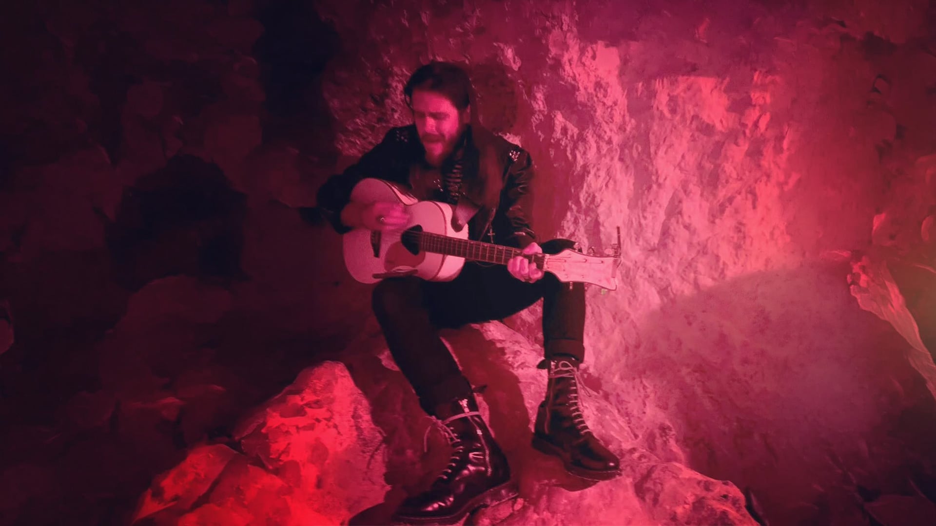Man playing acoustic guitar in red-lit rocky cave