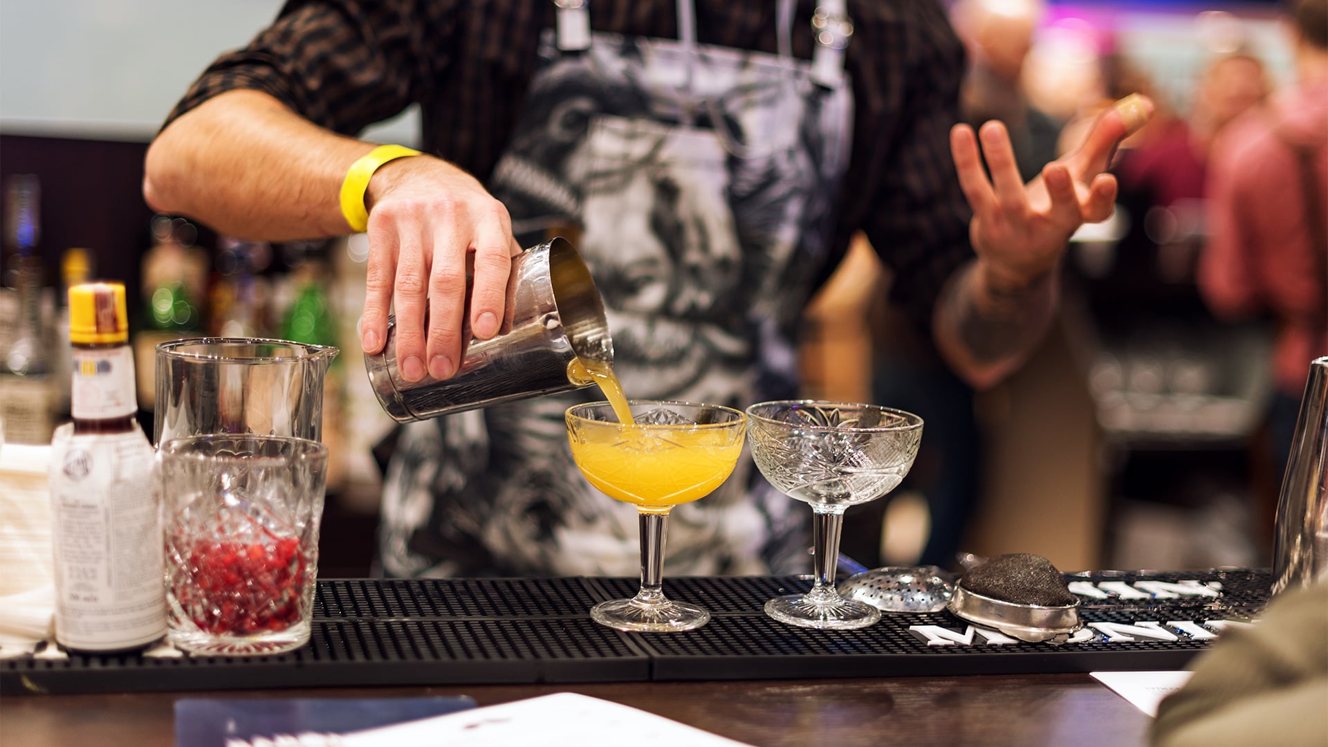 Bartender pours orange cocktail into a coupe glass
