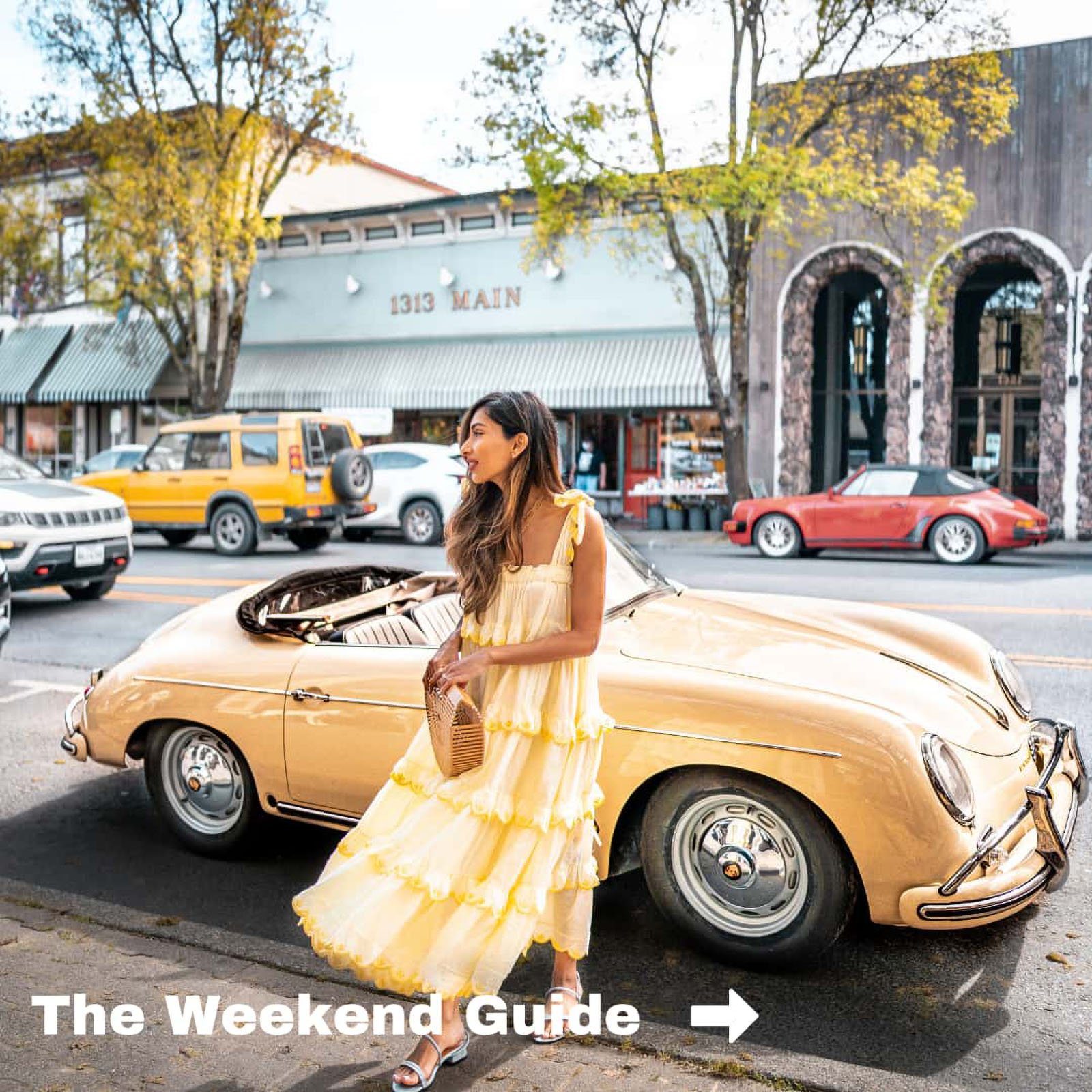 Woman in yellow dress beside vintage car, city street.