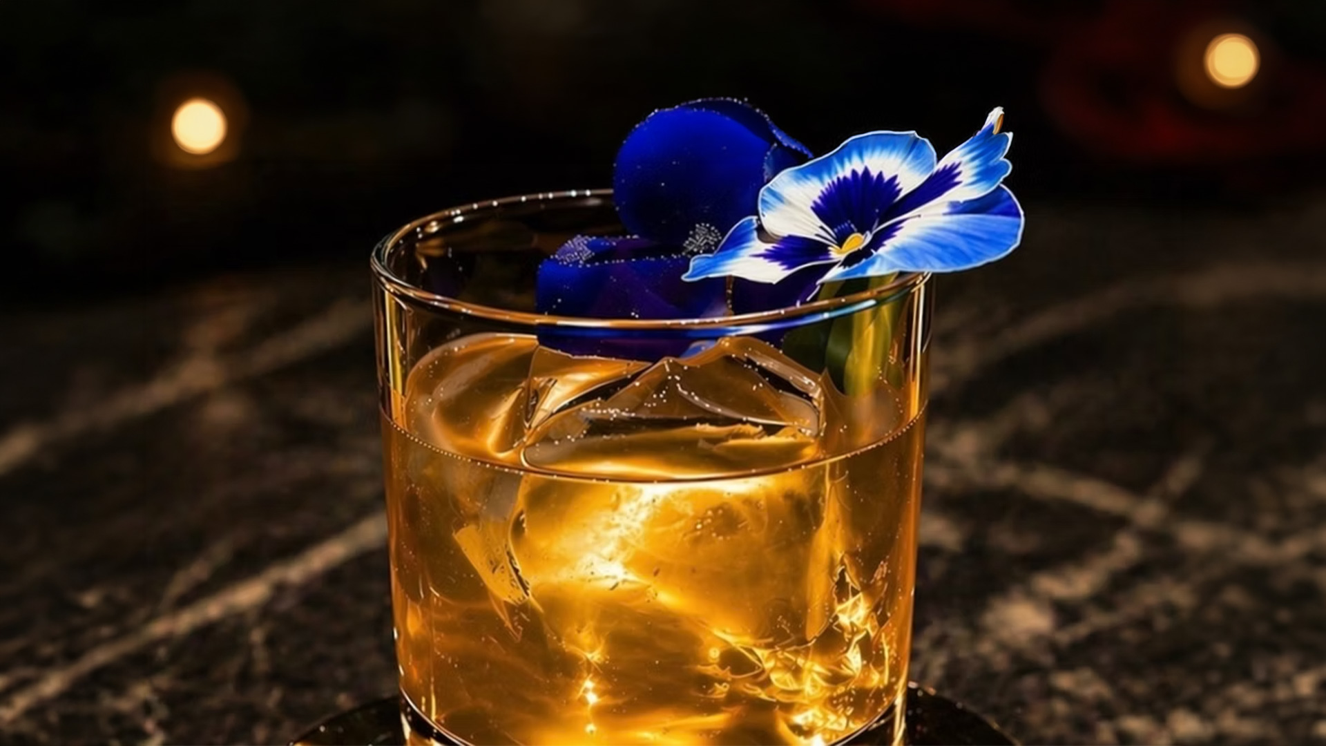 Whiskey cocktail with blue flower garnish and ice