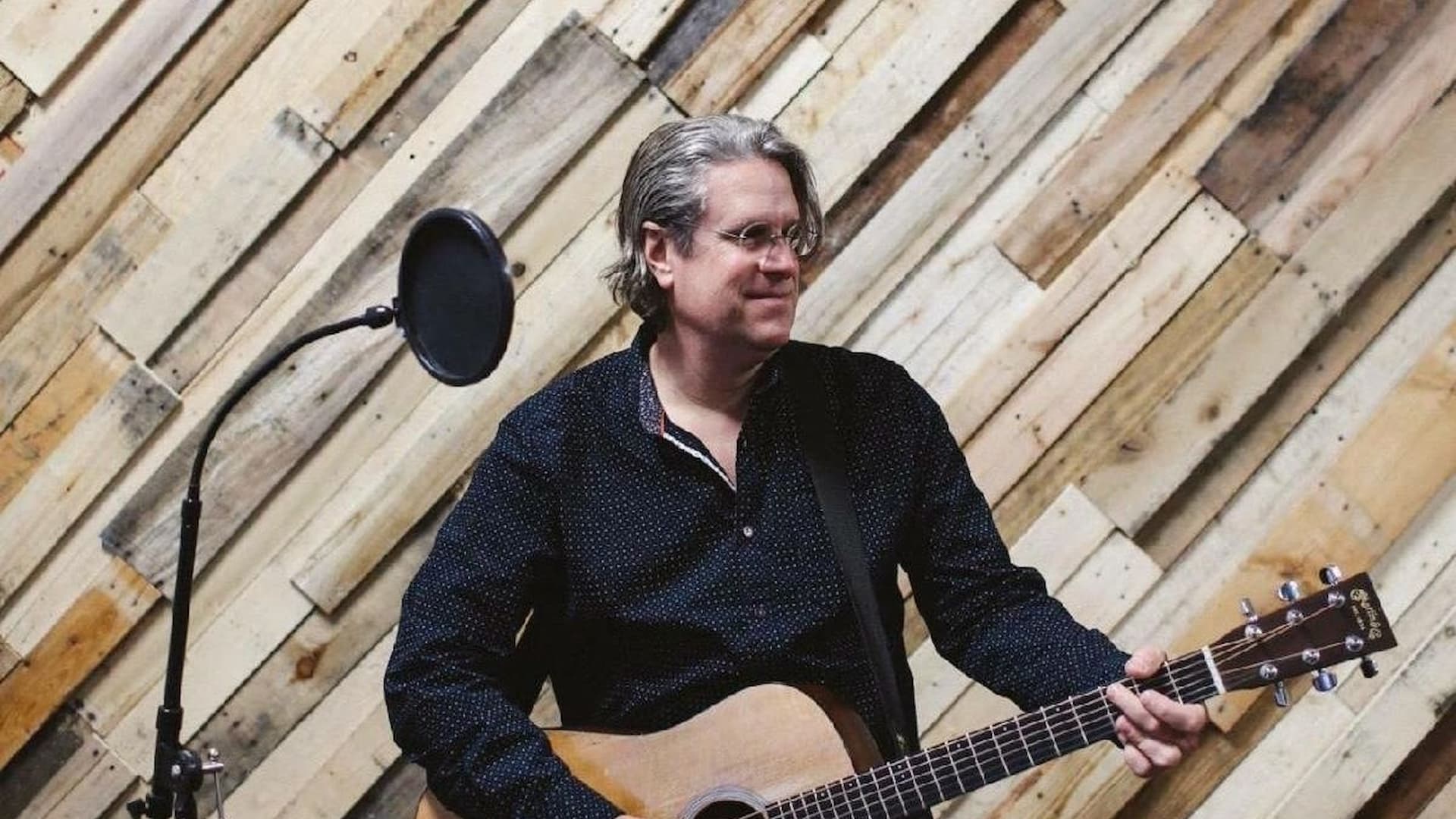 Man playing acoustic guitar beside microphone