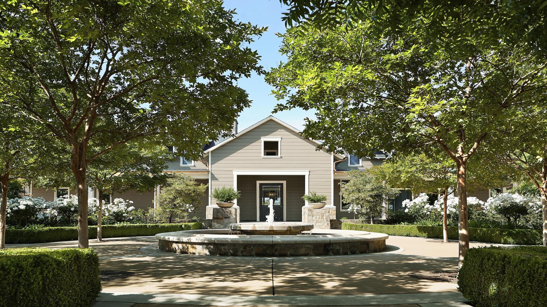 House with fountain and trees in front yard.