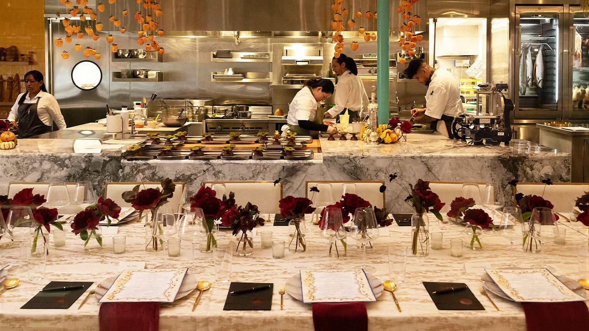 Chefs prepare dishes behind an elegantly decorated dining table.