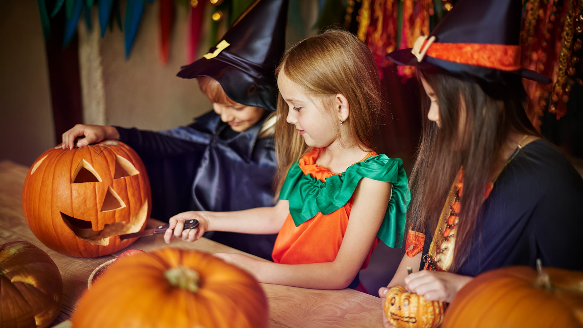 Children in costumes carve a jack-o'-lantern together.