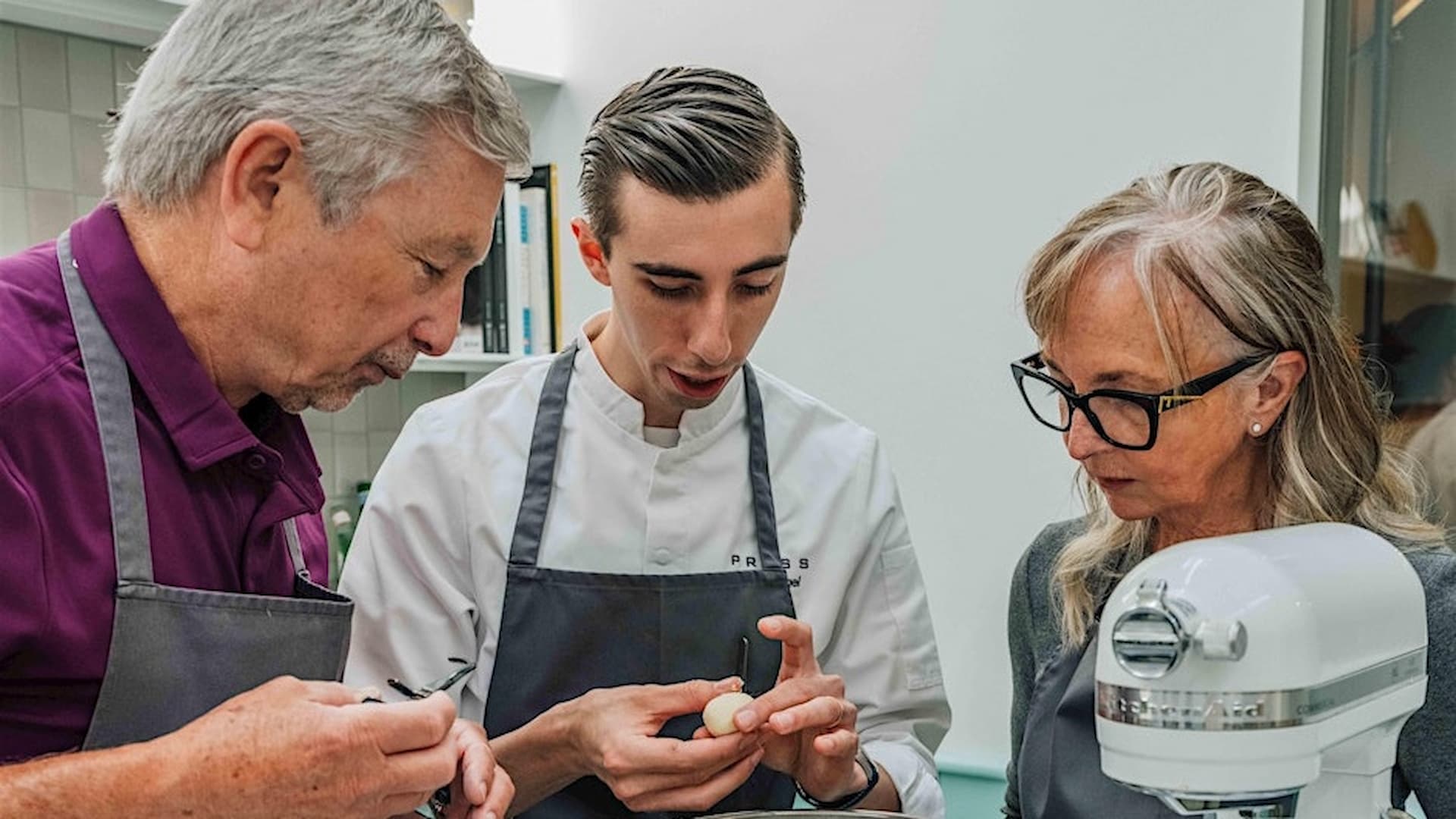 Chef demonstrates baking technique to two students.