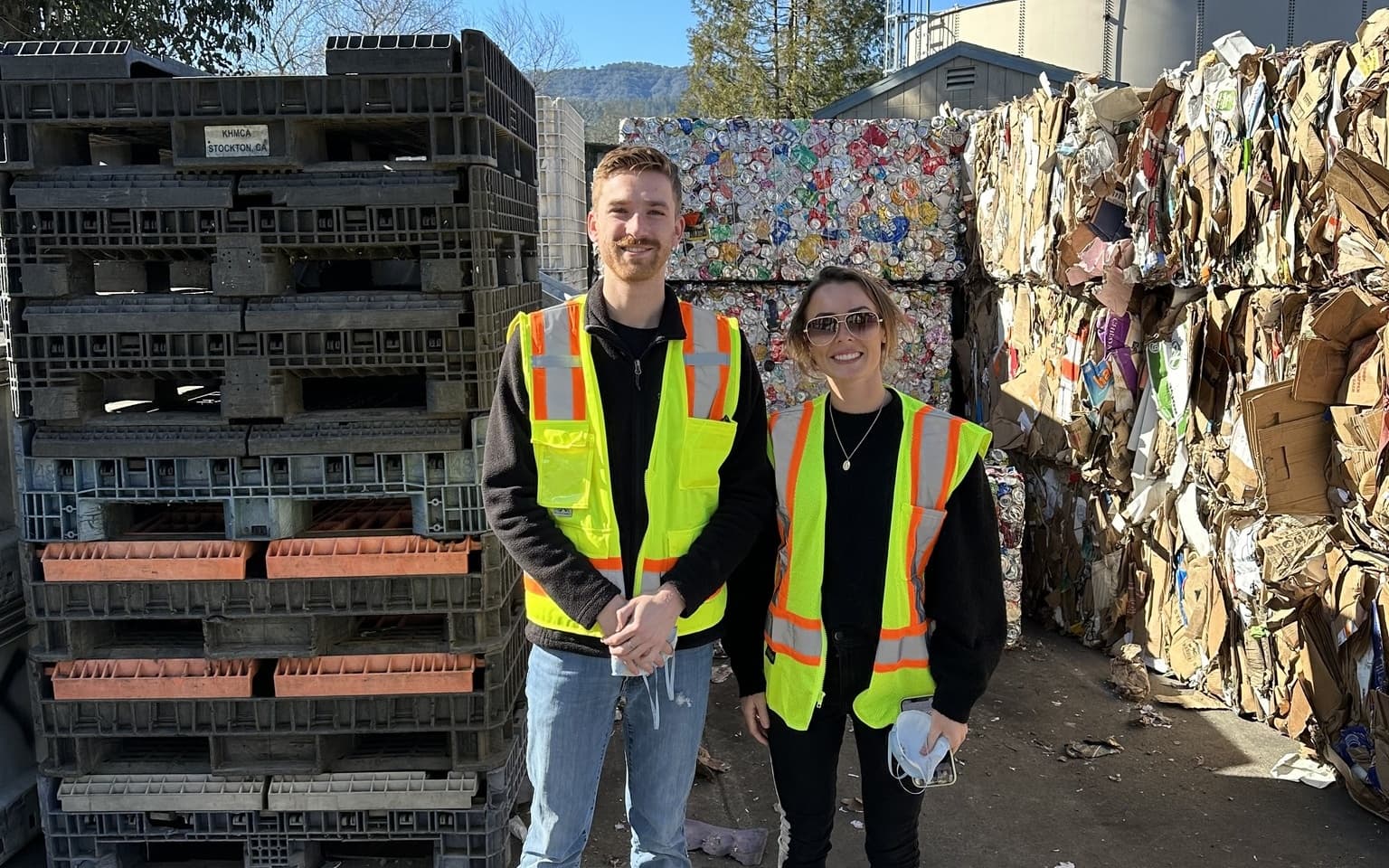 Two people in safety vests at recycling facility.