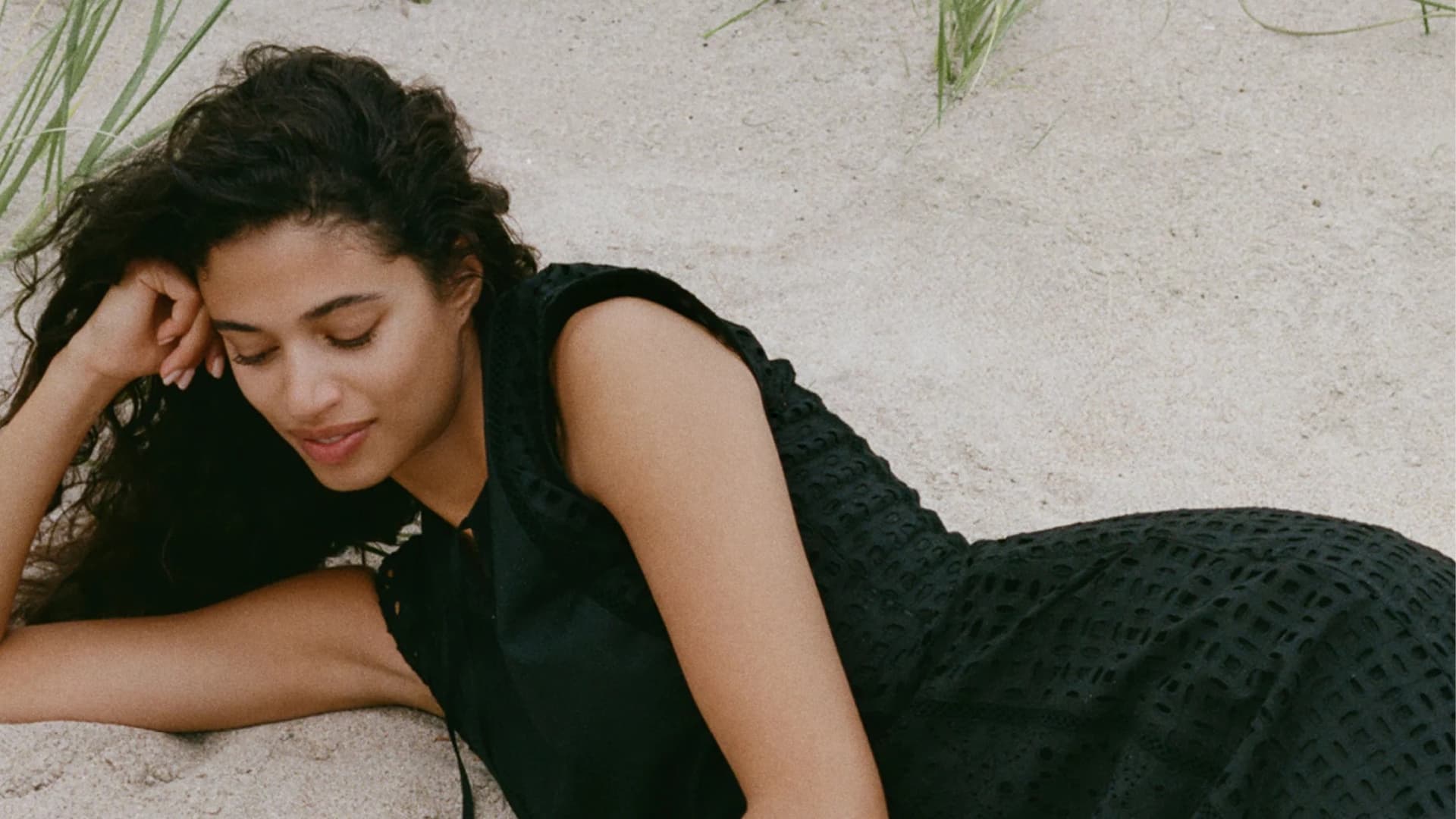 Person in black dress laying on sandy beach.