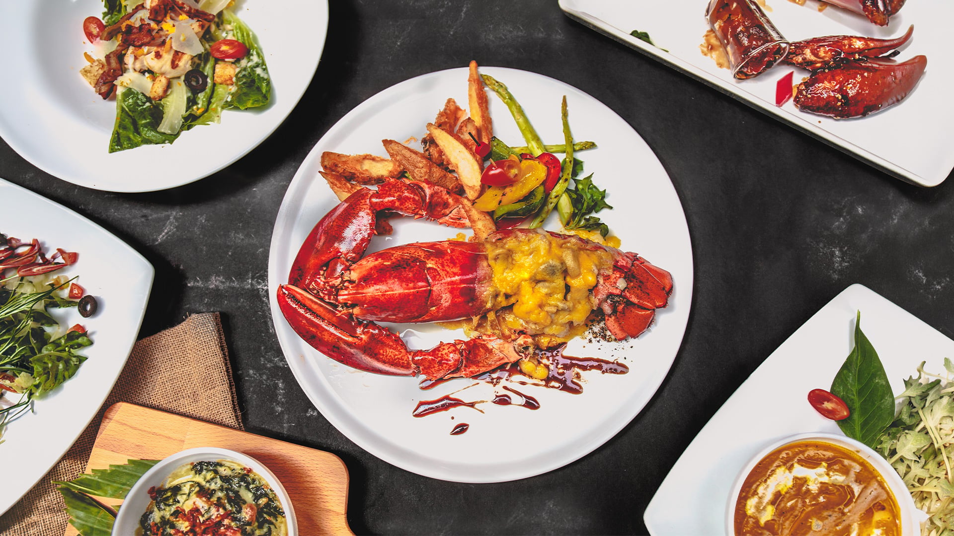 Plated lobster with vegetables, fries, salads, and soup