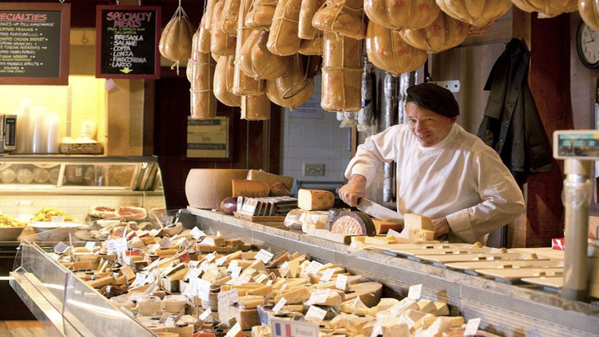 Cheese shop worker slicing cheeses.