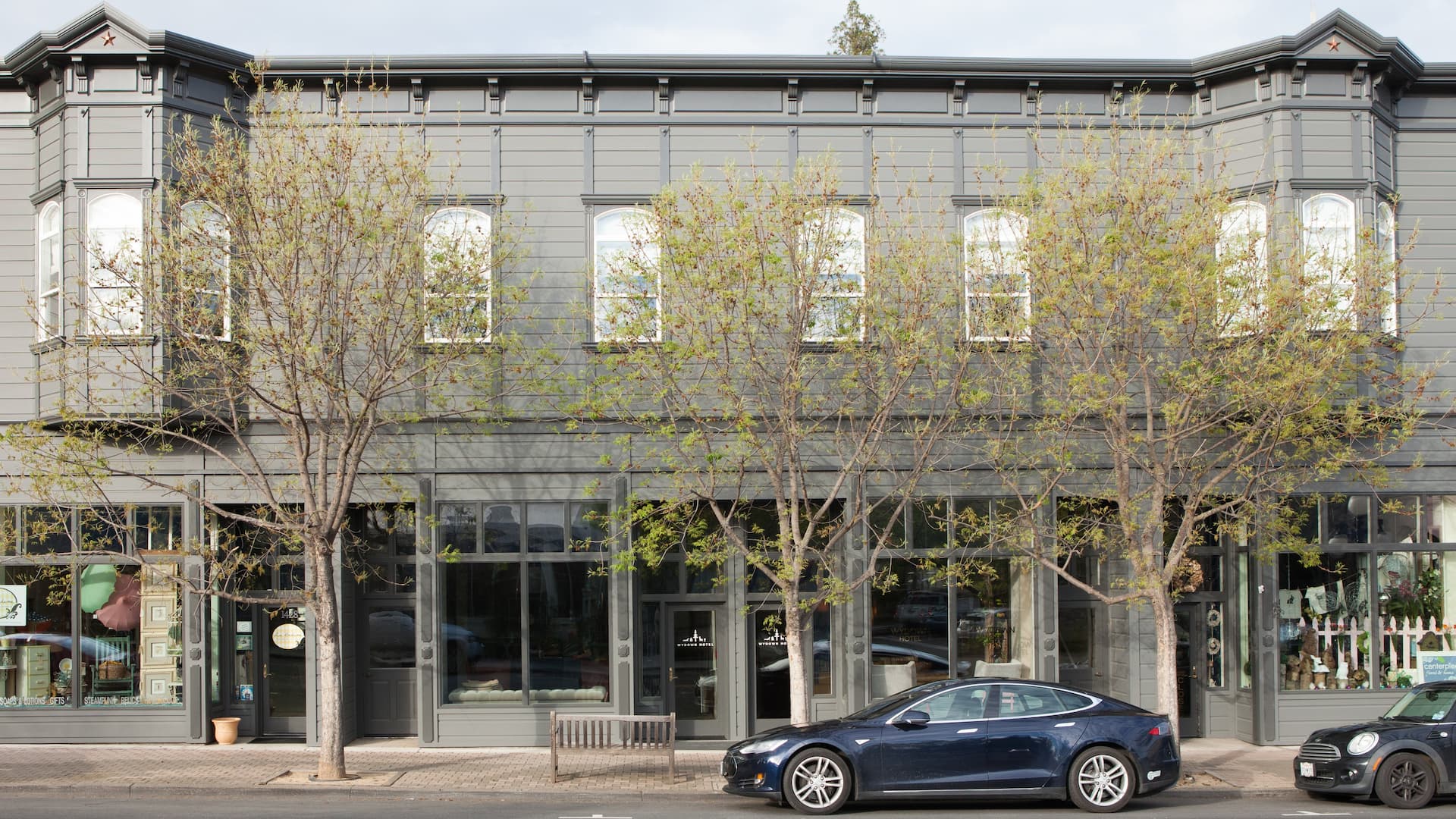 Historic gray building with parked cars and trees.